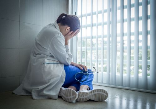 A depressed young female doctor sitting in despair near a hospital window - healthcare and sorrow concept