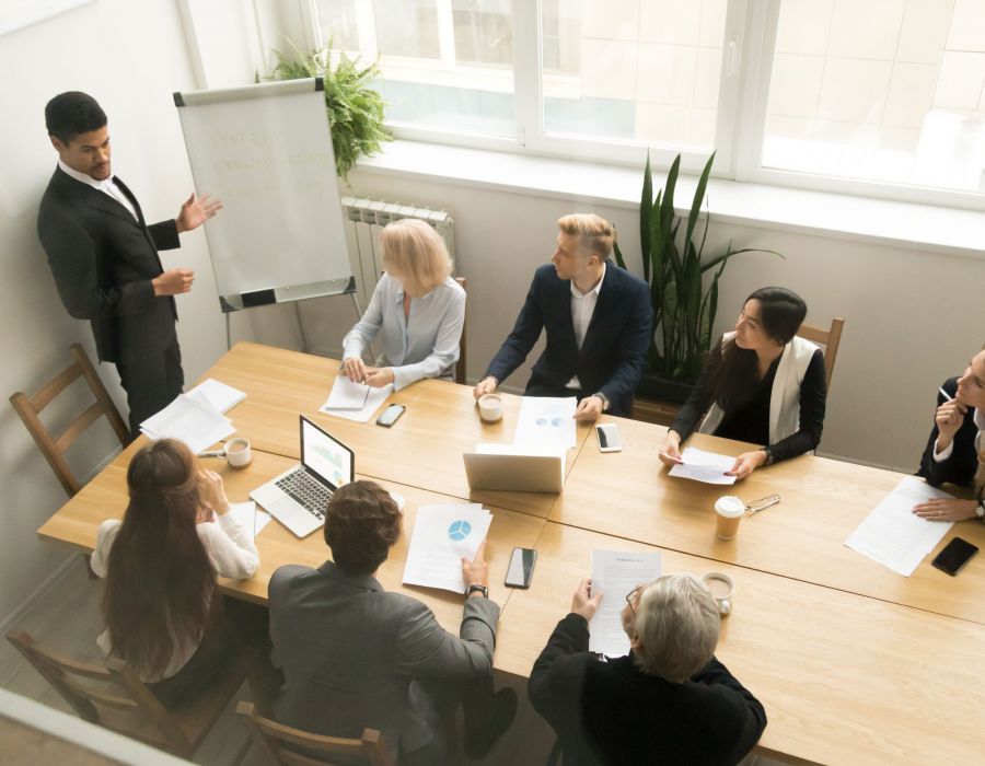 African american ceo boss in suit giving presentation at corporate team meeting concept, diverse executive group listening to black speaker explaining new plan coaching employees in conference room